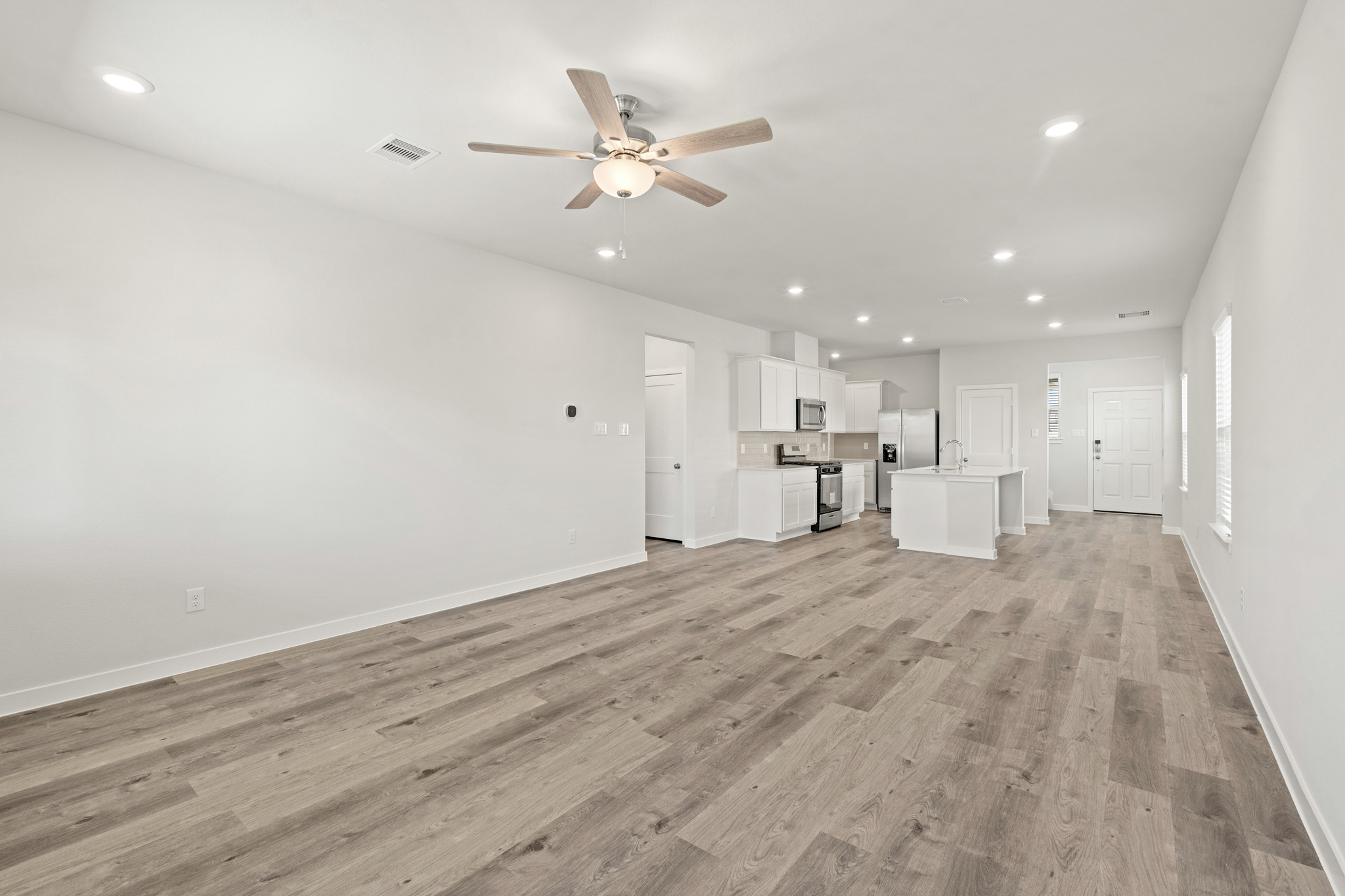 A large empty room with a ceiling fan and white cabinets.
