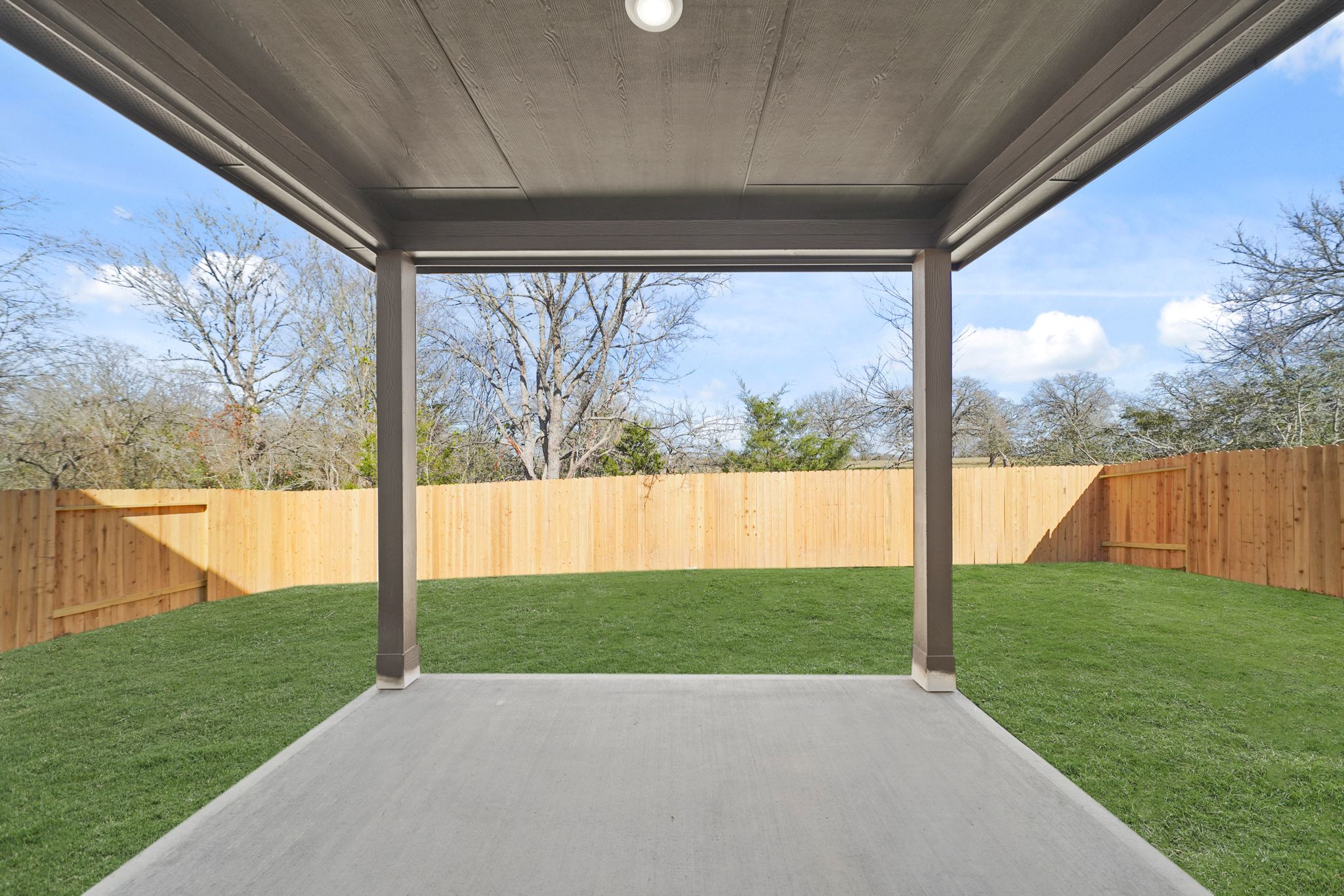 A covered patio with a fence and grass and trees with Glass House in the background.