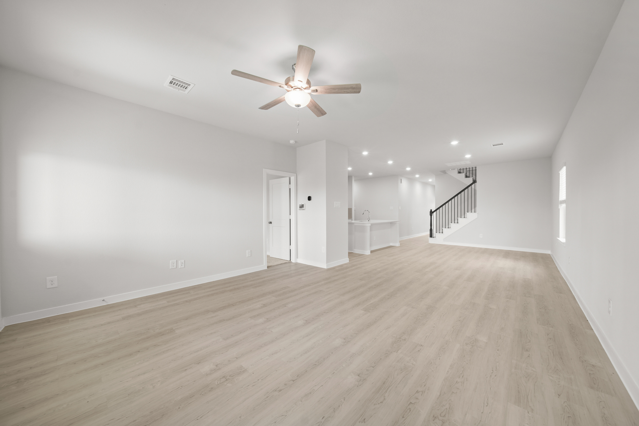 A large empty room with a ceiling fan and a wood floor.